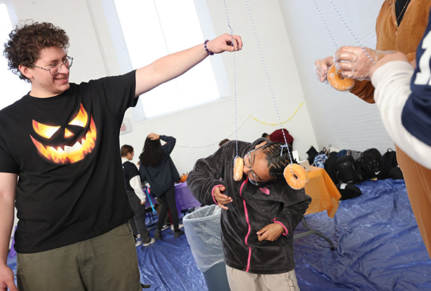 student holding a donut on a string while a child tries to bite it
